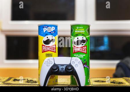 White gaming console controller on a table with potato chips cans. Stock Photo