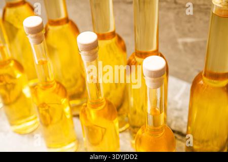 Bottles of homemade fruit liqueurs made from lemon, quince, pear, apple, white plum, peach, and apricot arranged in closeup on a marble surface. Stock Photo