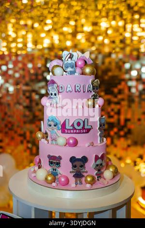 Three-tiered pink birthday cake with dolls and custom name topper on golden sequin background wall Stock Photo