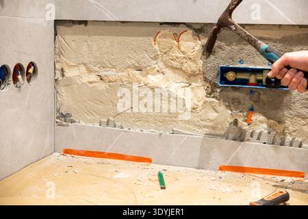 Close-up of bathroom wall showing removed damaged tile and exposed concealed plumbing element for sink faucet with hand holding crowbar during renovat Stock Photo