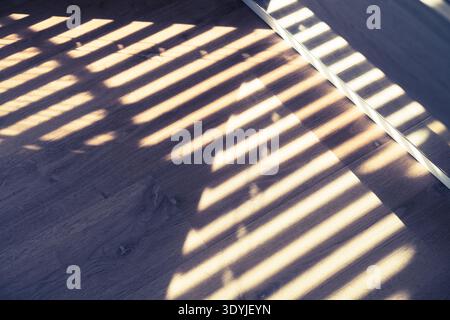 Close-up of a wooden floor showing installed hidden baseboard trim with sunlight casting striped shadows across the surface. Stock Photo