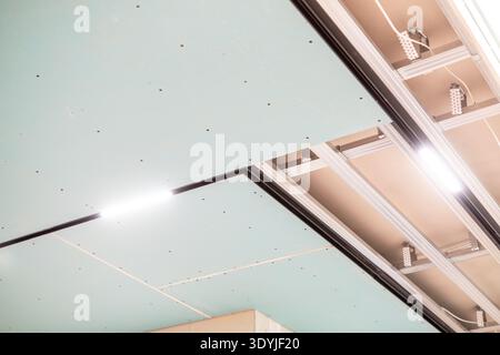 Close-up of suspended ceiling installation showing LED strip lighting and aluminum mounting tracks in a modern interior setting. Stock Photo