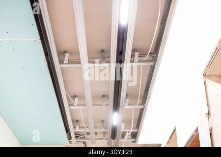 Modern suspended ceiling installation featuring illuminated track lighting with visible metal framework and integrated LED lights in a construction se Stock Photo
