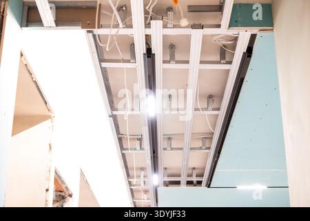 Under construction modern interior ceiling with exposed led track lighting and hidden ventilation grilles in drywall panels. Stock Photo