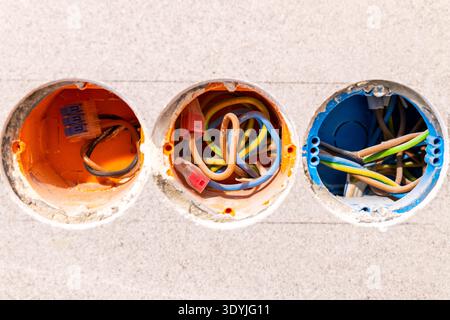 Three circular electrical boxes embedded in a wall with various colored insulated wires inside each box. Stock Photo