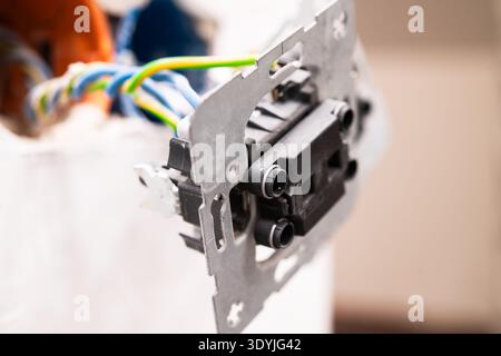Closeup view of an electrical outlet with exposed wiring and metal mounting bracket installed in a wall opening. Stock Photo