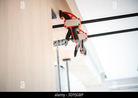 Two red and black pipe clamps securing wooden boards together in a workshop with bright natural lighting and industrial elements. Stock Photo