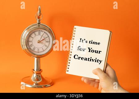 It's time for Your creativity. Business and financial concept. Notebook with a slogan in hand. Stylish clock and beautiful orange background Stock Photo