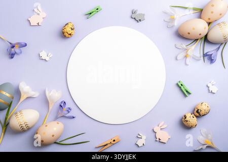 Easter eggs and rabbit decorations with crocus flowers around circle frame on purple background. Top view, flat lay, mockup. Stock Photo