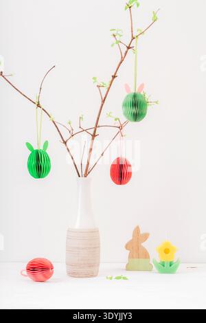 Multicolored decorative honeycomb-shaped Easter eggs hanging on a branch. A ceramic vase on a white wooden table. Happy Easter concept, greeting card. Stock Photo
