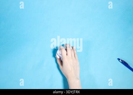 top view of hand holds ball of paper and pen on blue paper background Stock Photo