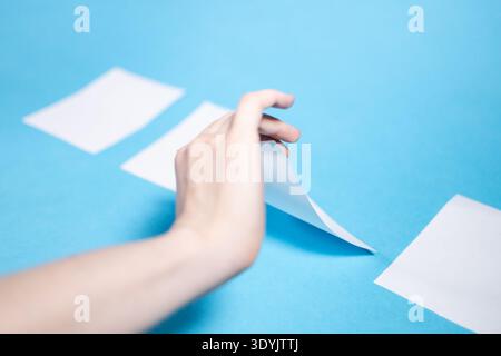 hand lifts one sheet of paper from four sheets on blue paper background Stock Photo