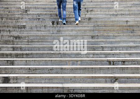 Two pairs of legs ascending a flight of stone stairs Stock Photo