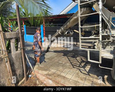 A dedicated construction worker carefully pours fresh concrete on a foundation in Bang Lamung, Thailand. Stock Photo
