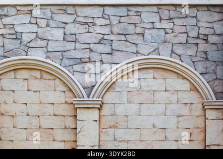 A textured stone wall features decorative arches and a combination of different masonry styles. Architectural detail, wall texture, masonry work. Stock Photo
