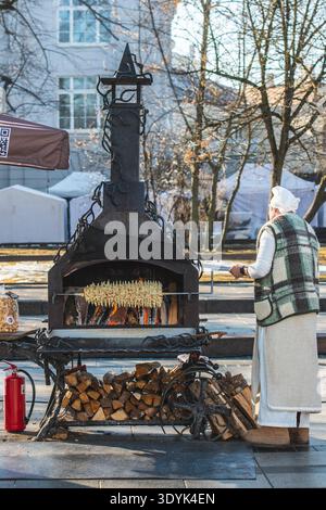 Woman in traditional clothes preparing Lithuanian tree cake, šakotis or baumkuchenas, Polish sękacz, Belarusian bankucha, German baumkuchen Stock Photo