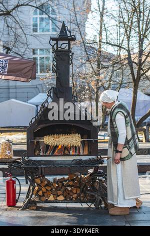 Woman in traditional clothes preparing Lithuanian tree cake, šakotis or baumkuchenas, Polish sękacz, Belarusian bankucha, German baumkuchen Stock Photo