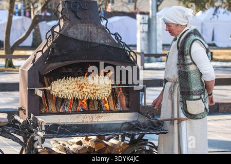 Woman in traditional clothes preparing Lithuanian tree cake, šakotis or baumkuchenas, Polish sękacz, Belarusian bankucha, German baumkuchen Stock Photo