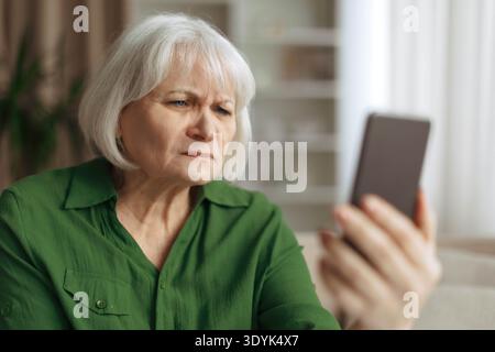 Senior woman squinting eyes while looking at smartphone screen Stock Photo