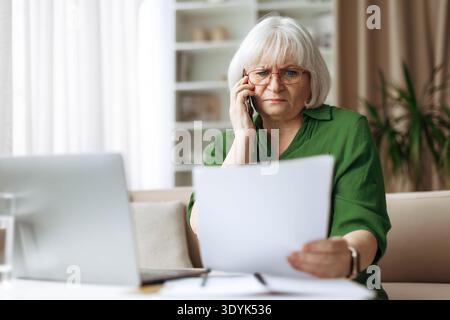 Senior woman talking on phone while checking documents at home Stock Photo