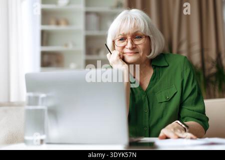 Senior woman looking at laptop screen with thoughtful expression at home Stock Photo