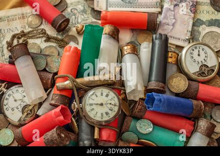 a collection of vintage and discarded items, on antique pocket watches and used shotgun shells, scattered among old coins, banknotes, and metal chains Stock Photo