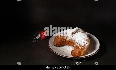 Fresh baked butter croissant on white ceramic plate with sugar powder strawberry  on vintage brown background. Bakery or pastry shop card with copy sp Stock Photo