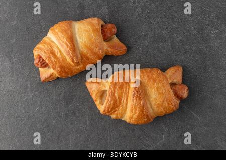 Sausage croissants closeup on dark stone table background. Sausages in puff dough on grunge stone background Stock Photo