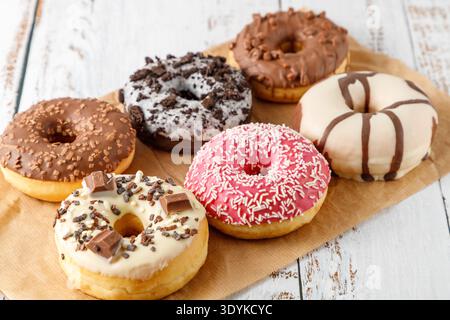 Set of assorted colorful white and dark chocolate glazed donuts with mixed sprinkles on paper on wooden table. Sweet pastry card. Fresh baked pink, br Stock Photo