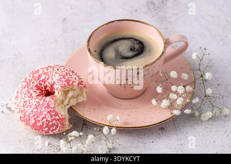 Biten pink glazed donut with sprinkles and vintage coffee cup closeup on stone table. Fresh baked doughnut as dessert for coffee break Stock Photo