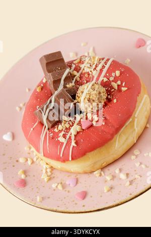 Sweet donut with red icing, chocolate pieces, candy and sprinkles on vintage pate closeup on yellow background Stock Photo