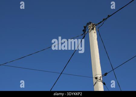 A tall utility pole stands against a blue sky with several power lines connected to it. The scene shows a clear day with no clouds in sight. Stock Photo