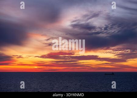 Baltic Sea sunset with cargo ship silhouette on the horizon beneath dramatic clouds, Baltic Sea, Northern Europe Stock Photo