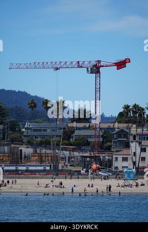 Santa Cruz, California, USA. ?July ?24, ?2023. A crane is standing on a beach near a town. The crane is red and tall. There are many people on the bea Stock Photo