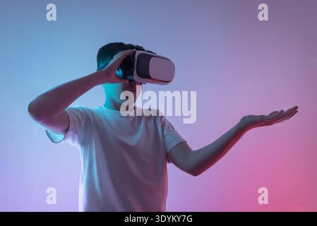 Teen boy wearing virtual reality headset holding open hand as if presenting futuristic hologram dashboard or digital data interface, augmented reality Stock Photo