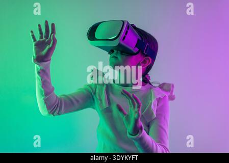 Child wearing virtual reality headset exploring immersive digital world with colorful lighting representing metaverse technology, gaming experience an Stock Photo