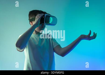 Teen boy wearing virtual reality headset holding open hand as if presenting hologram interface, futuristic augmented reality concept with copy space f Stock Photo