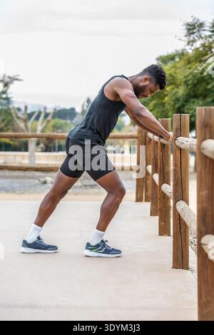 Full body side view of young African American male athlete in activewear stretching legs while warming up before training Stock Photo