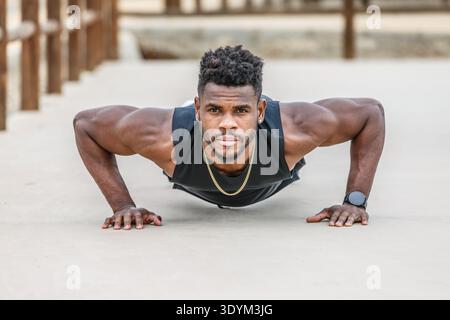 Strong African American male athlete in sportswear with Afro hair doing push ups on ground during functional training Stock Photo