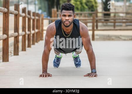 Full body of concentrated young African American athlete with muscular arms doing plank exercise on ground during fitness workout in summer park Stock Photo