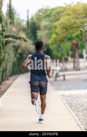 Back view of unrecognizable black athlete in sportswear running in park during active cardio exercise on summer weekend Stock Photo