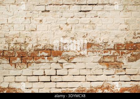 Aged brick wall with flaking white paint, cracks and exposed bricks creating gritty vintage texture. Perfect for grunge or architectural backgrounds. Stock Photo