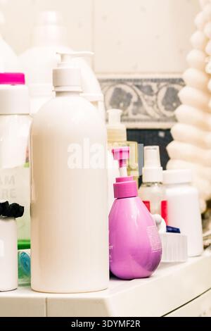 White and purple soap dispensers surrounded by assorted personal care bottles on tiled bathroom background Stock Photo