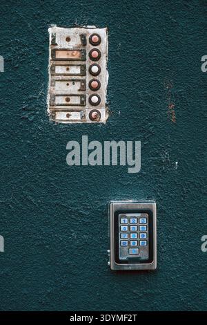 Close-up of vintage door intercom and contemporary keypad on teal concrete surface, showing decay, rust and technology contrast in urban architectural Stock Photo