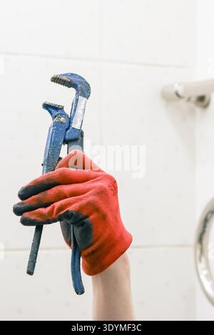 Vertical shot of manual worker holding used pipe pliers with tiled bathroom background and metal rail Stock Photo