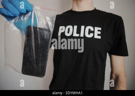 Police officer in gloves with a smartphone into an evidence bag. Concept of data security and cybercrime Stock Photo