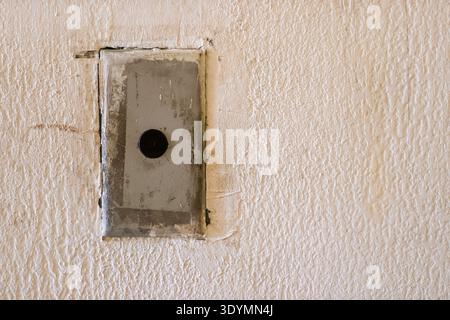 Close-up of an aged, weathered doorbell switch mounted on a rough, beige stucco wall in an old building. Stock Photo
