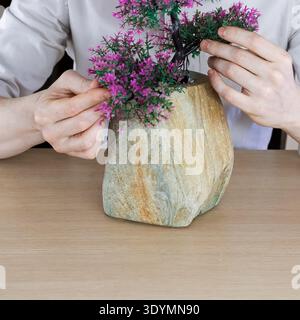 Hands gently touching and arranging purple-flowered decorative tree in textured pot. Stock Photo