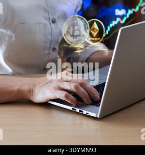 Man's hand on laptop keys, screen featuring multiple digital coins and fluctuating charts. Stock Photo
