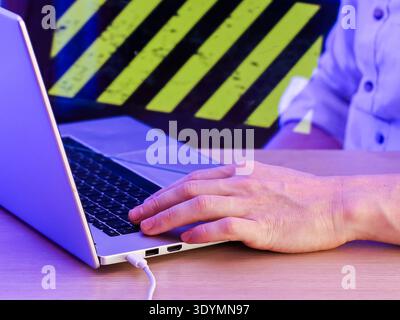 Person's hands typing on laptop in front of yellow-black diagonal caution stripes Stock Photo